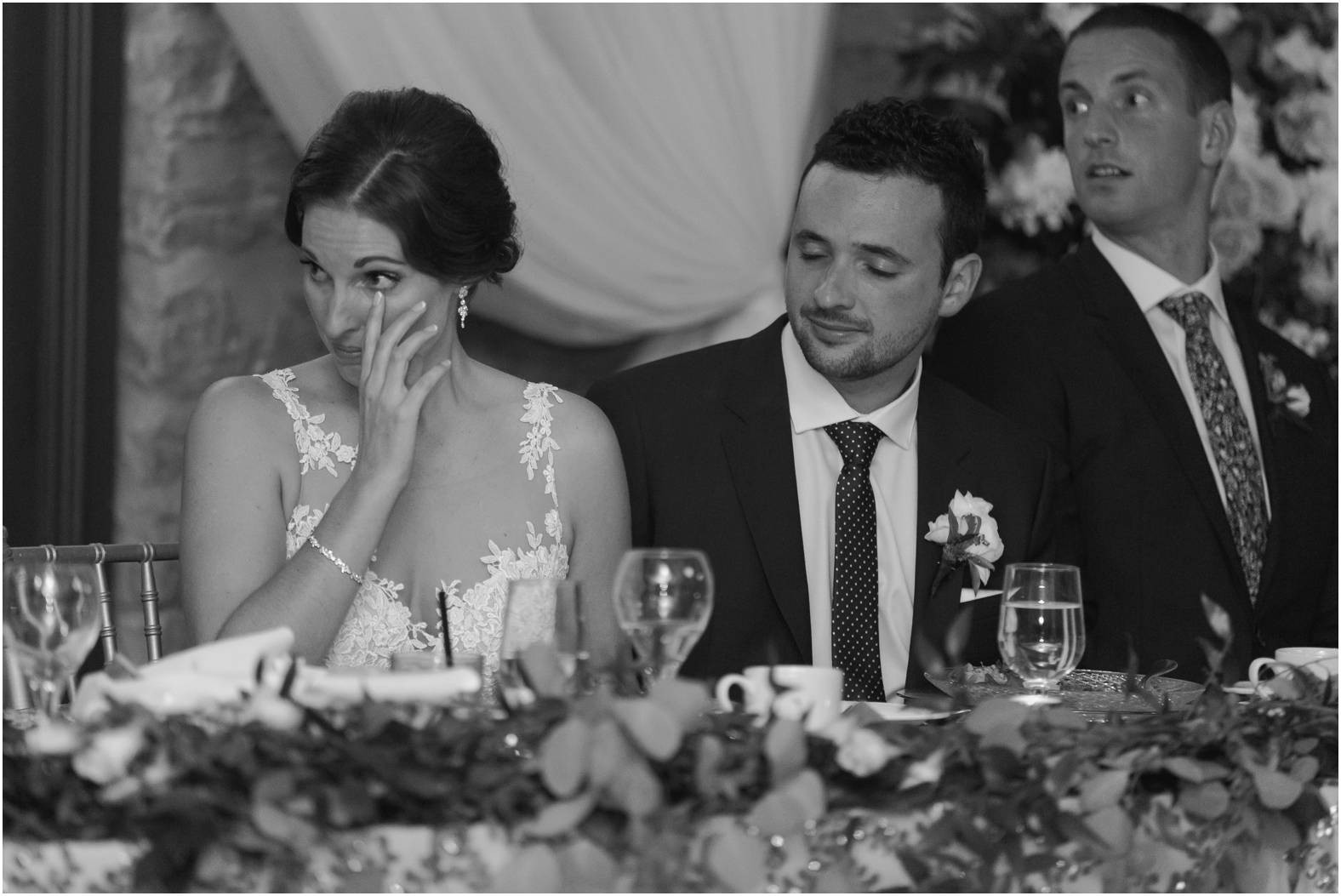 emotional black and white image of bride wiping tear during wedding speeches
