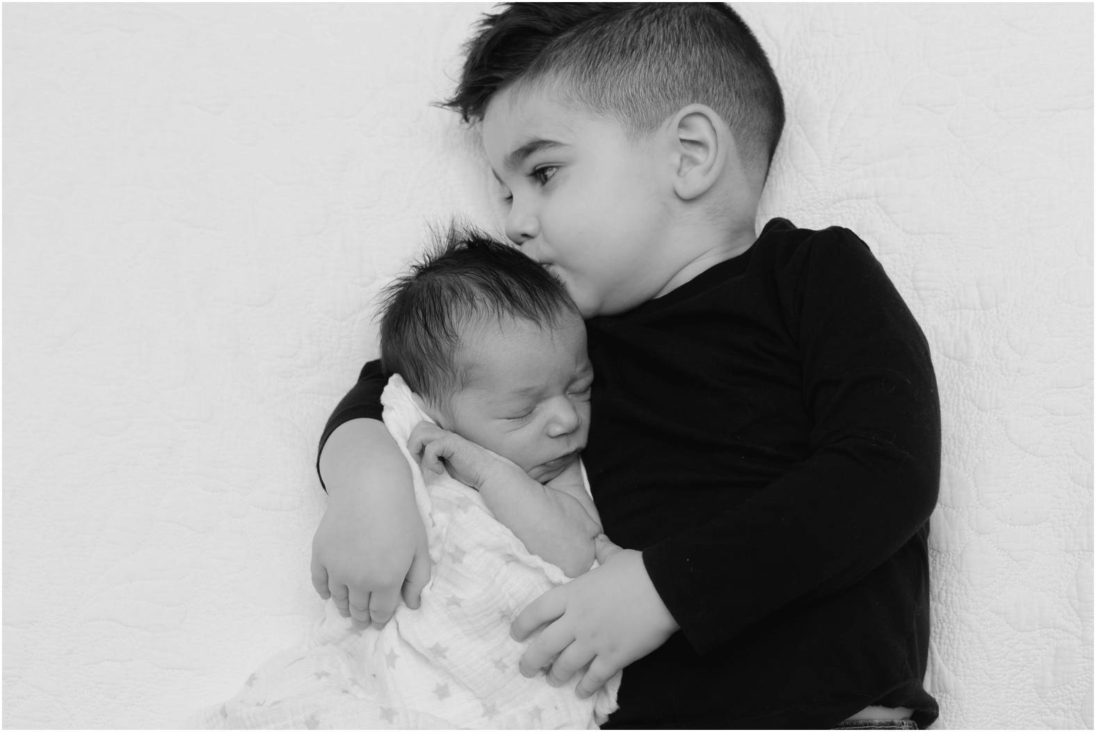 Black and white image of toddler boy snuggling his newborn baby brother