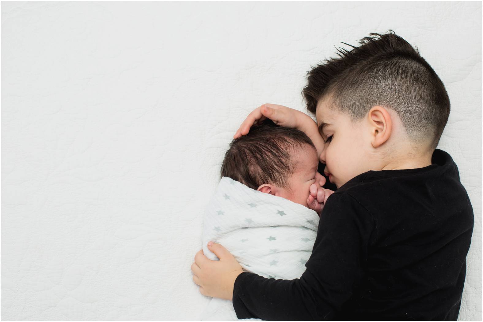 Black and white image of toddler boy snuggling his newborn baby brother