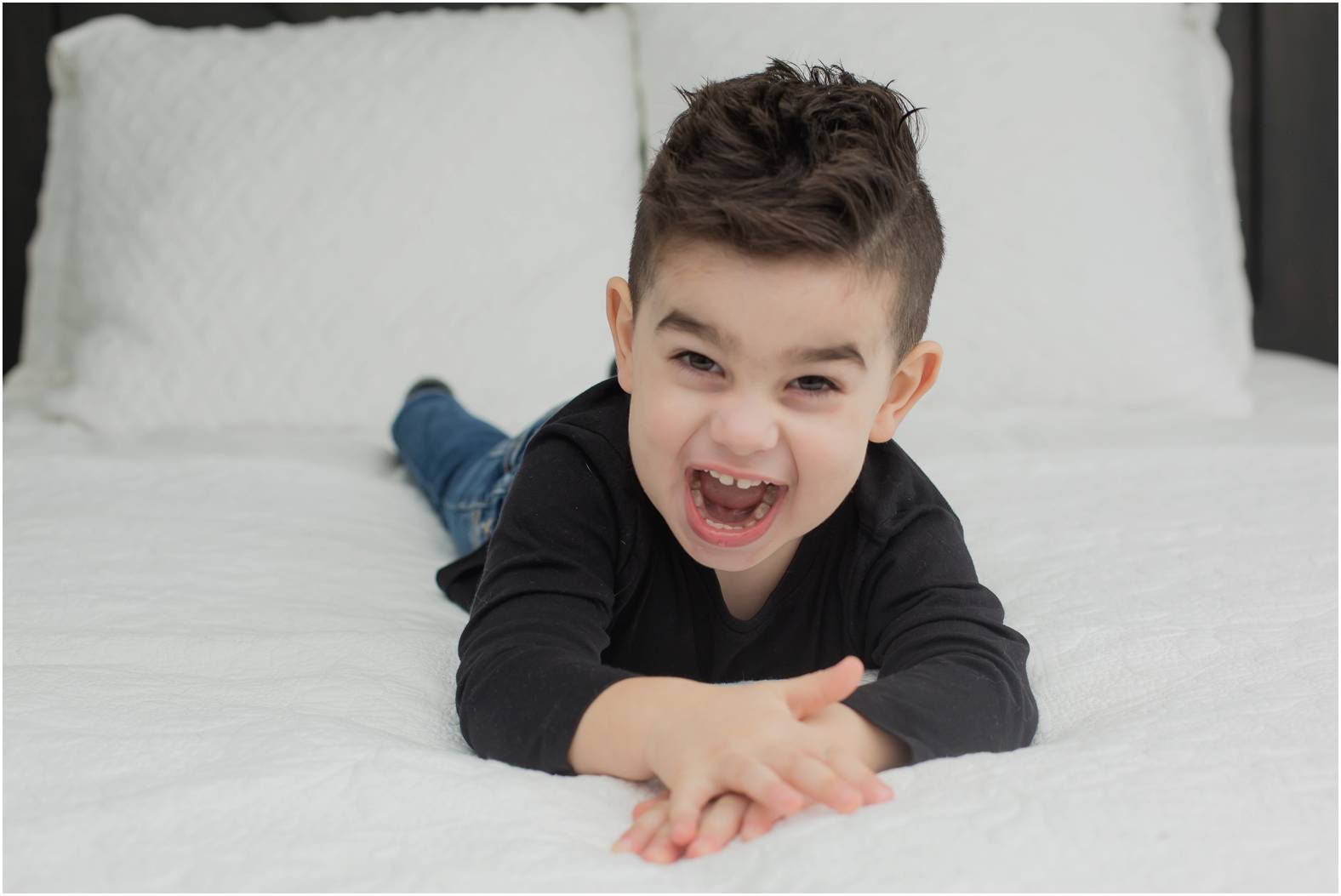 Toddler lies on bed and laughs during lifestyle newborn session.