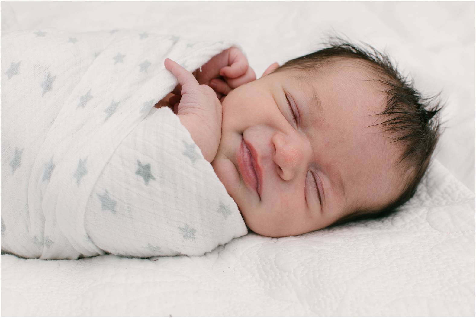 Newborn baby boy with dark hair swaddled in a neutral blanket