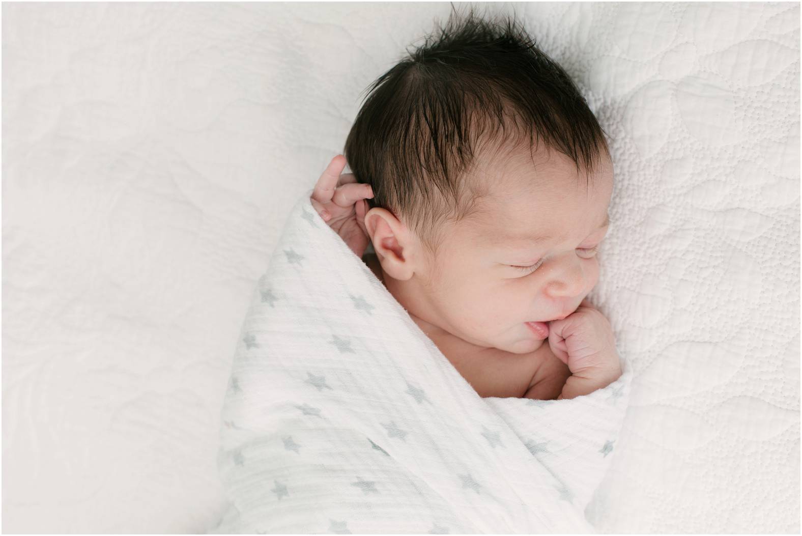 Newborn baby boy with dark hair swaddled in a neutral blanket