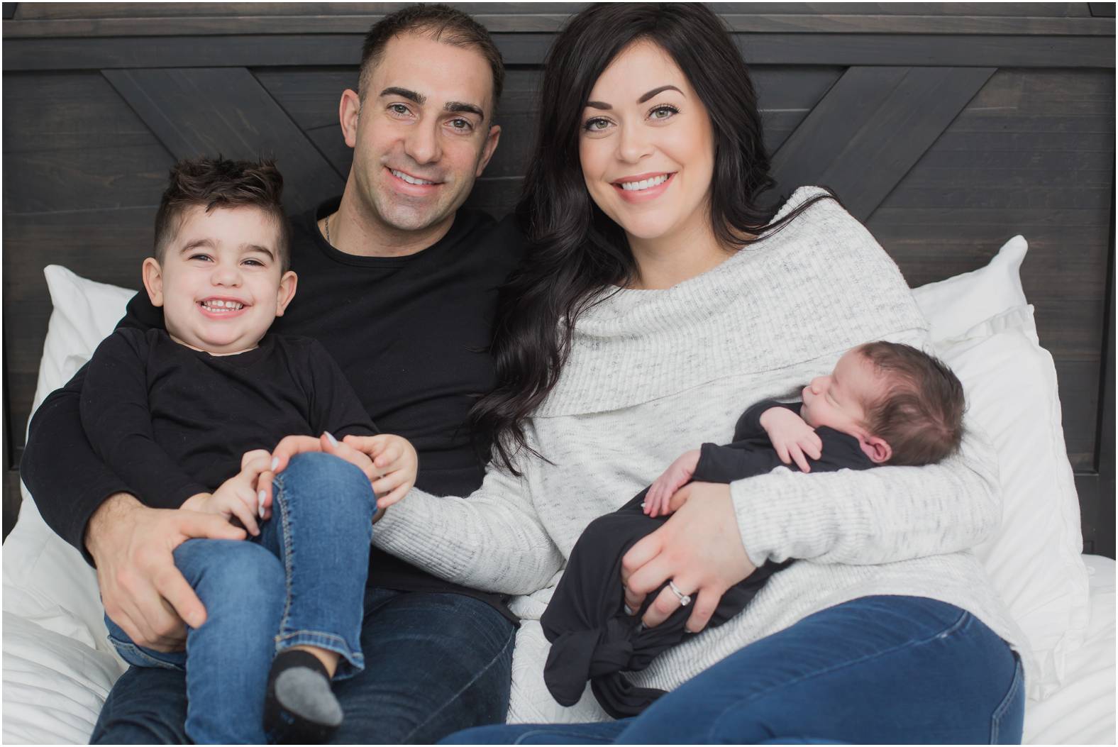 Family of four snuggle newborn baby boy on the bed during a newborn session