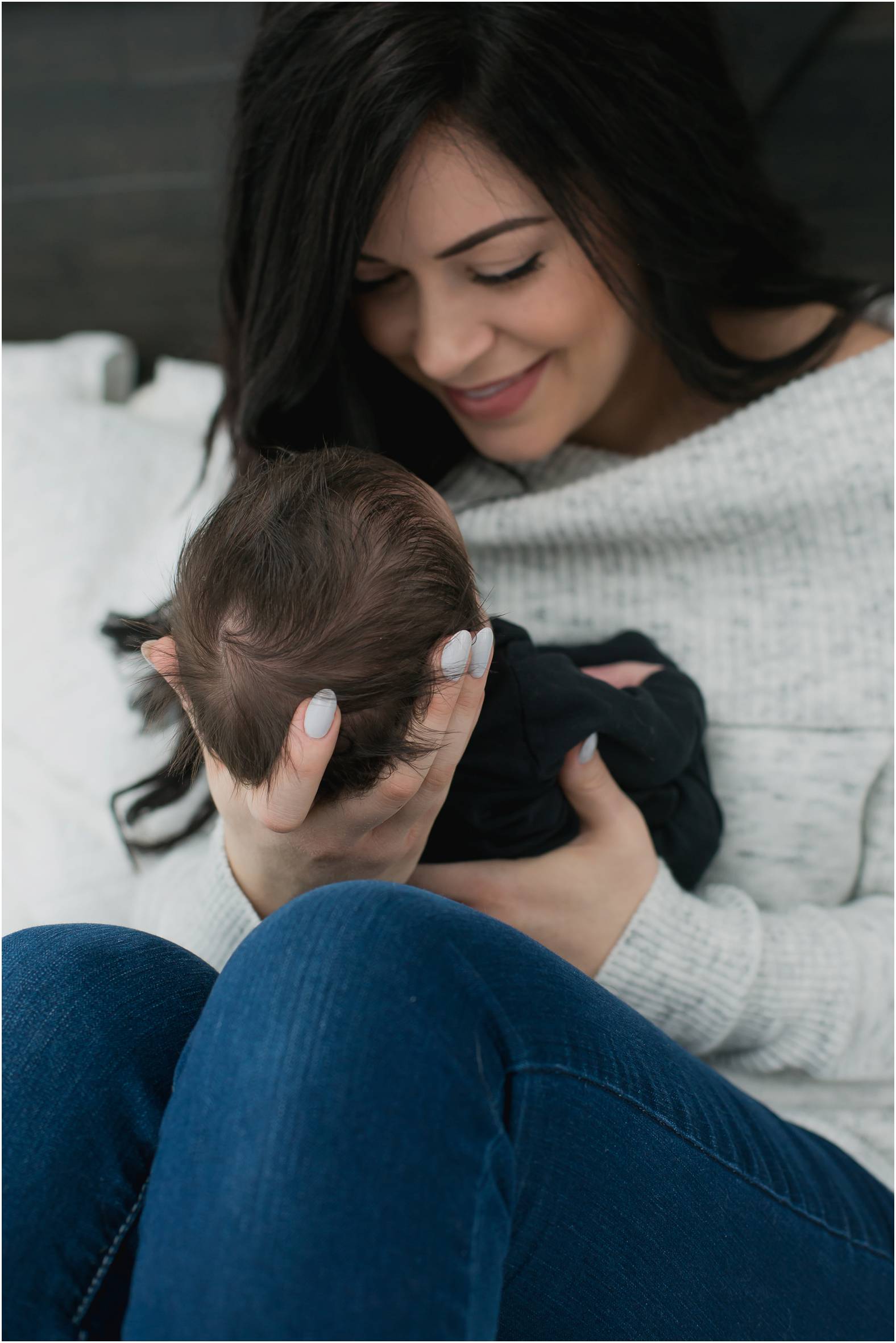 Mom snuggles newborn baby boy with lots of black hair.