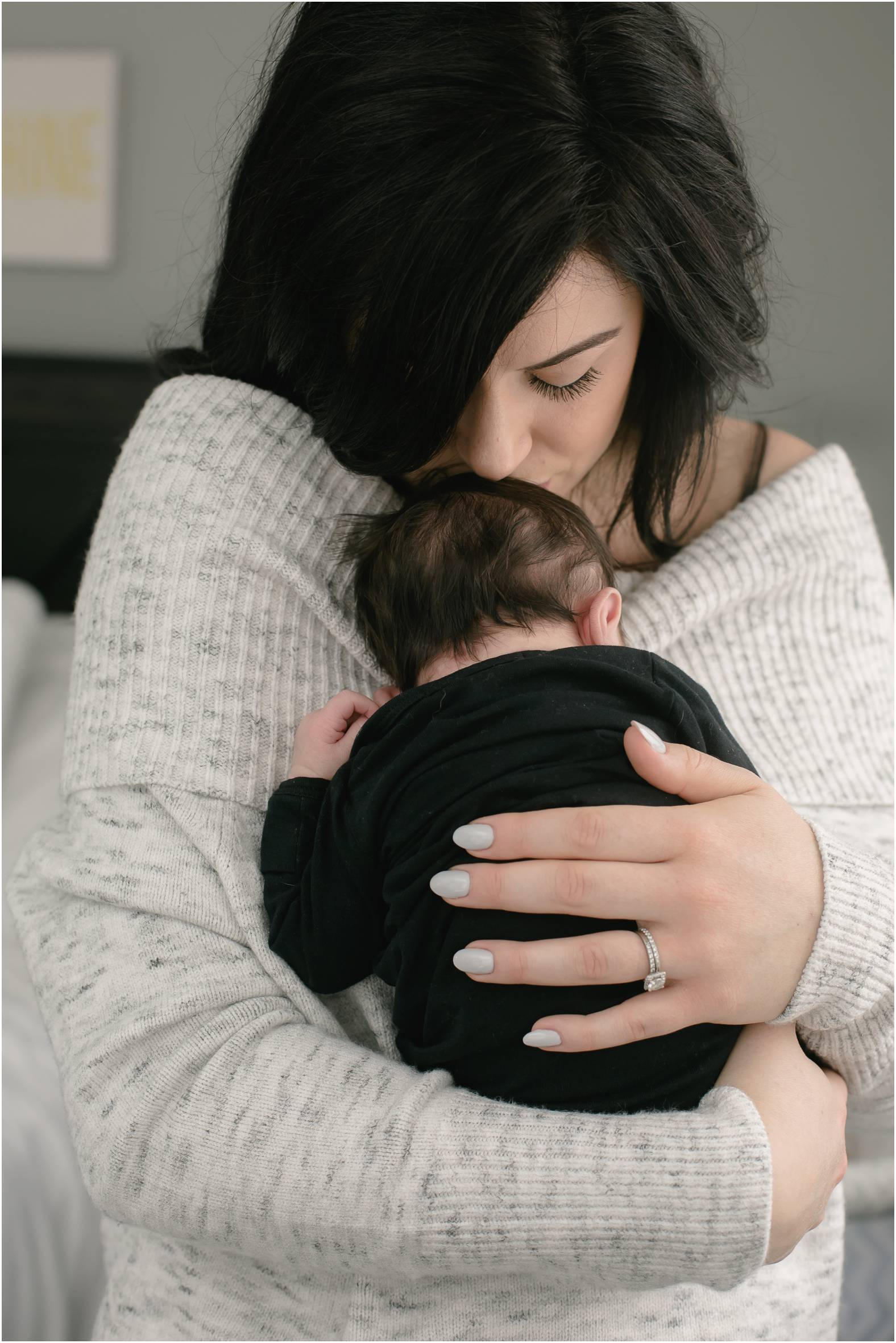 Mom snuggles newborn baby boy with lots of black hair to her chest
