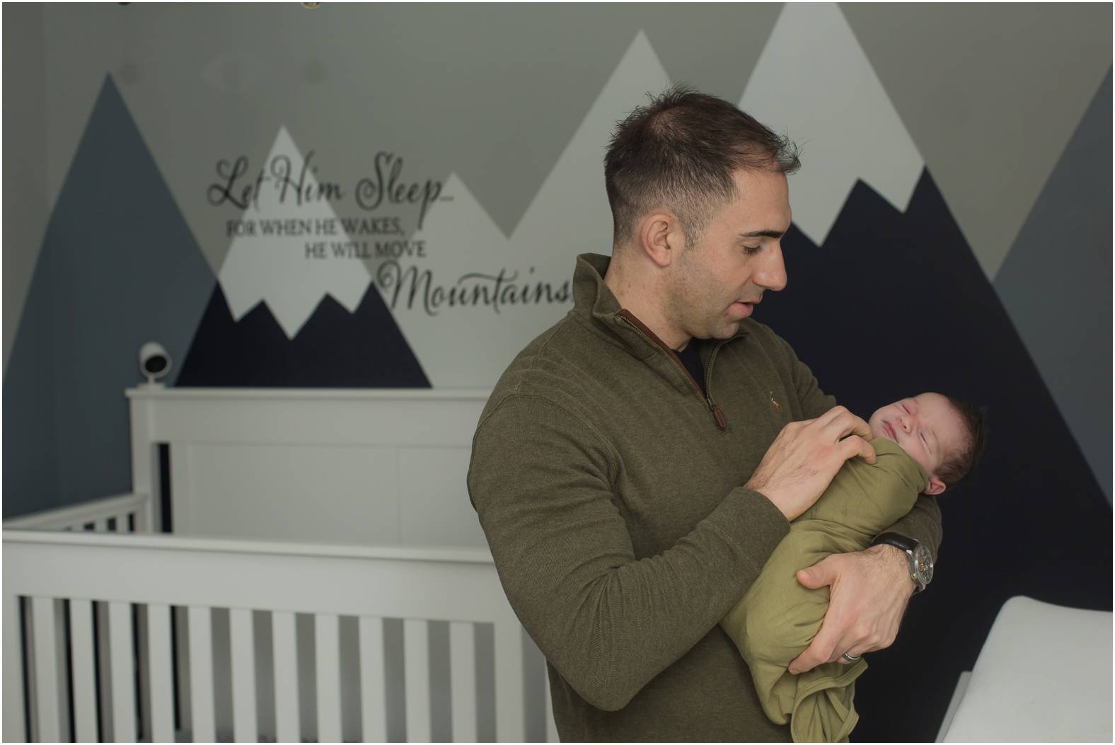 Dad snuggles newborn baby boy in nursery with mountain wall decal