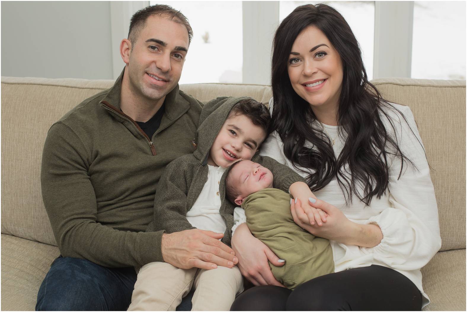 Family of four snuggle newborn baby boy on the couch during their inhome newborn session