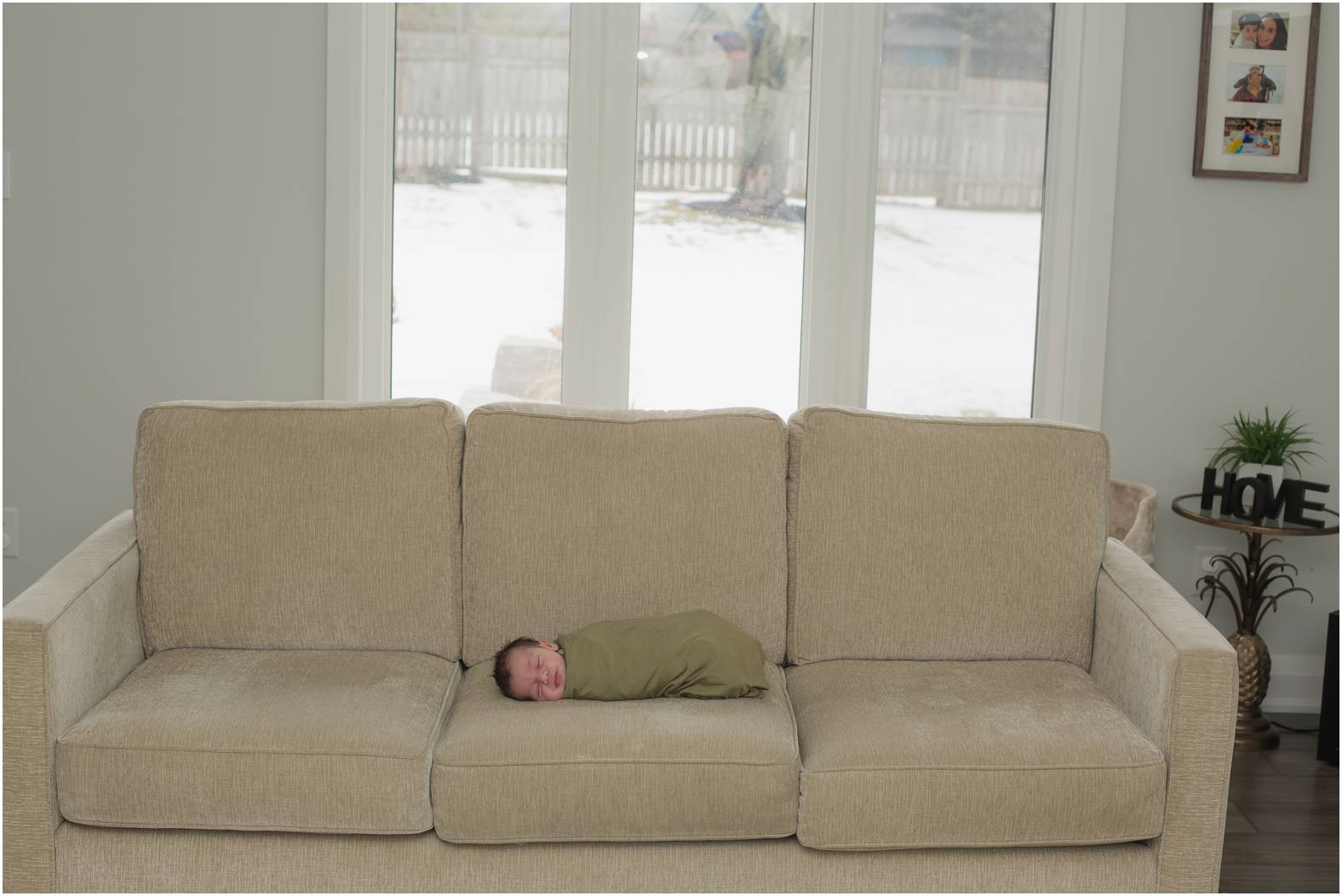 Newborn baby boy swaddled in an olive green blanket lies on the couch during his in-home newborn session.