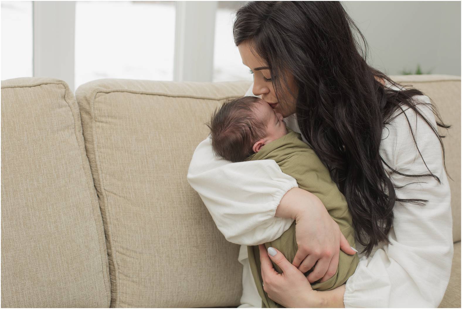 Mom snuggles newborn baby on the couch during his newborn portrait session.