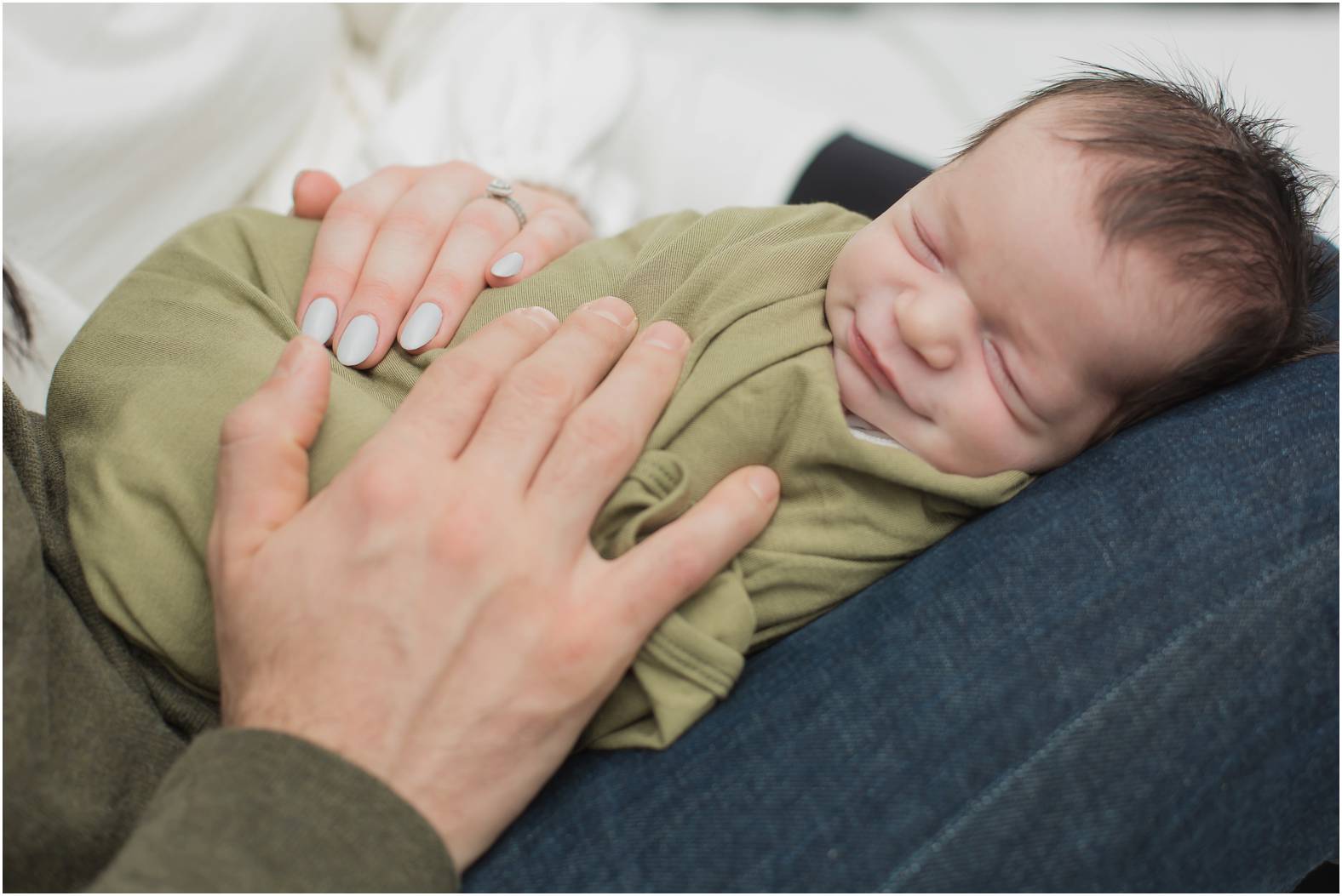 Dad snuggles newborn baby boy swaddled in olive green blanket on the bed.