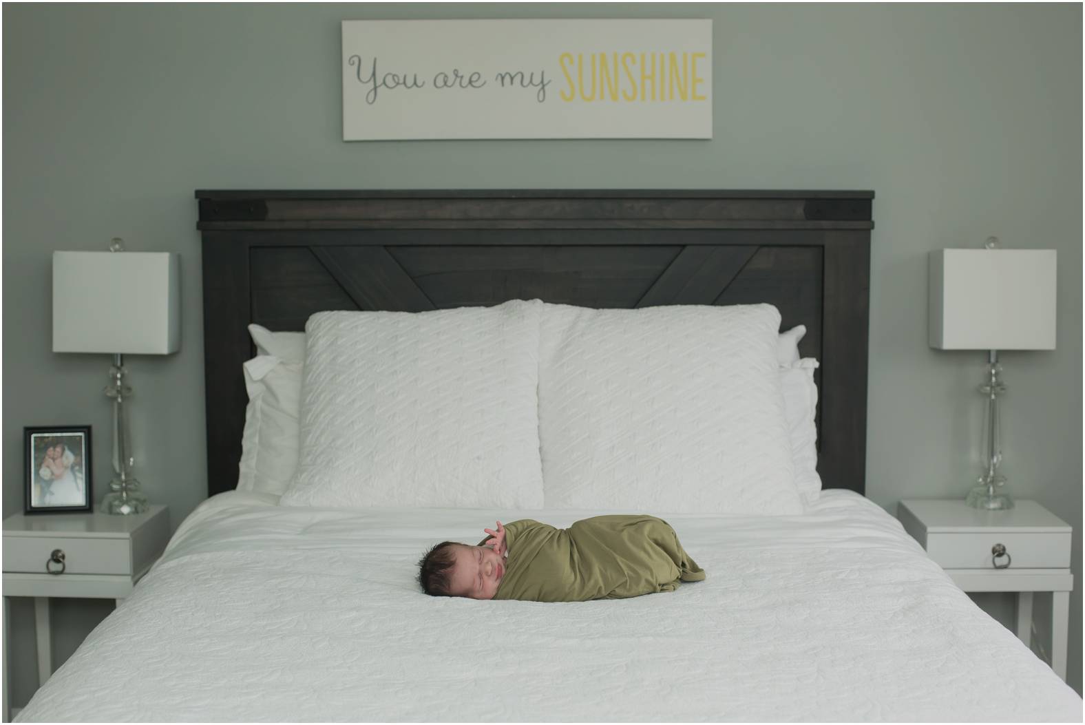 Newborn baby boy swaddled in olive green blanket on bed.