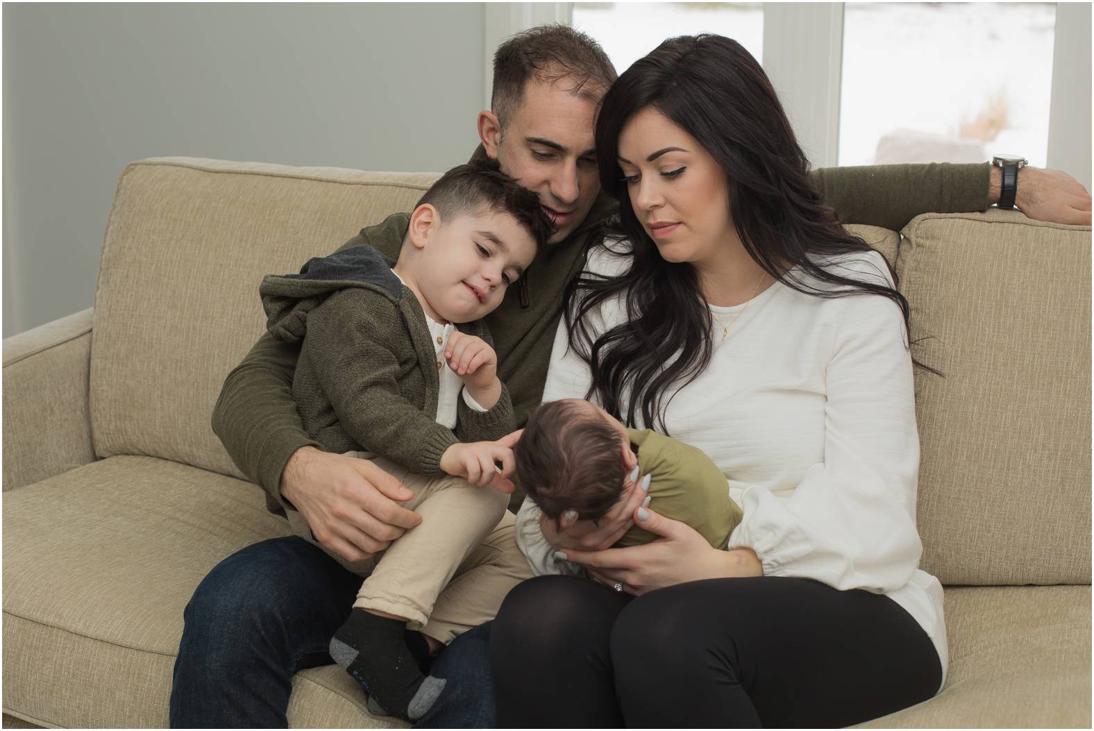 Family of four snuggle newborn baby boy on the couch during their inhome newborn session